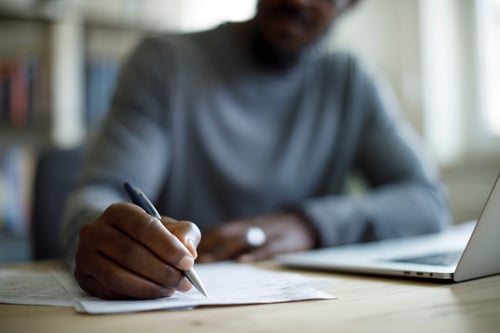 close up of someone writing on a document next to a computer