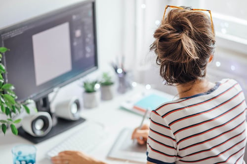 female professional writing in a notebook while working at a desktop computer