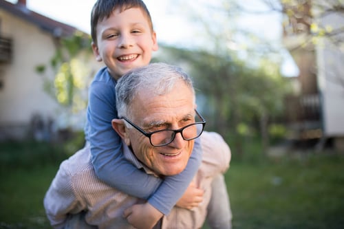 grandfather giving smiling grandson piggy back ride