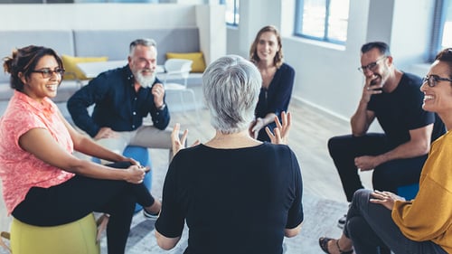 group of six adults sitting in a circle discussing and smiling in an office setting