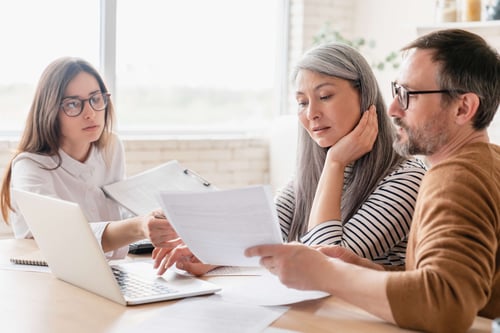 three worried people sitting together looking at a computer and documents