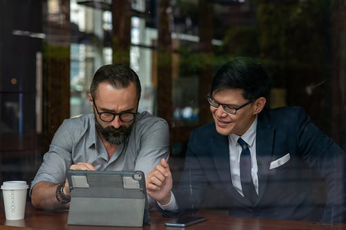two male professionals seated together looking at a tablet
