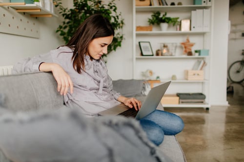 worried female looking at a laptop sitting on a grey couch
